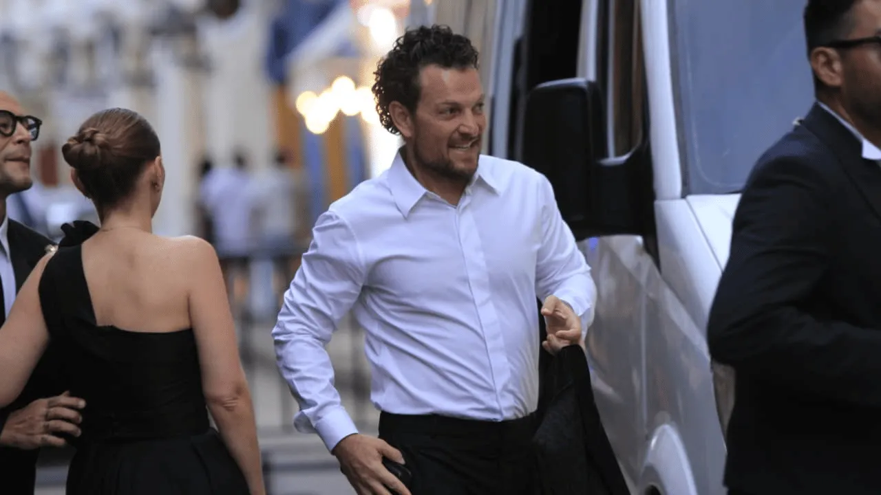 Hombre de cabello crespo y camisa blanca baja de una camioneta con un saco en la mano.
